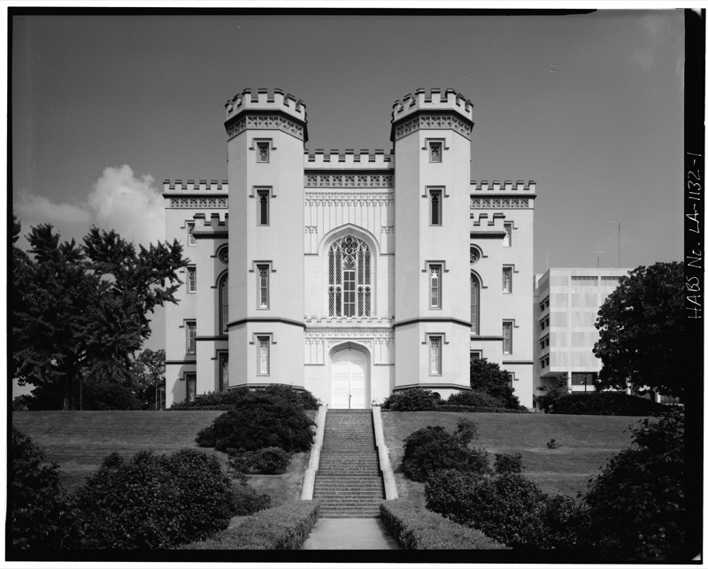 Black and white photograph of the castle-like Old State Capitol in Baton Rouge, with twin crenellated towers, a tall arched window over the main door, and a long staircase rising up a grassy terrace.